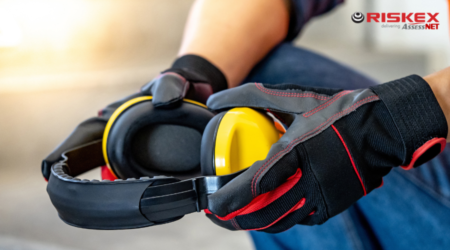 A worker wearing PPE gloves holding ear defenders.