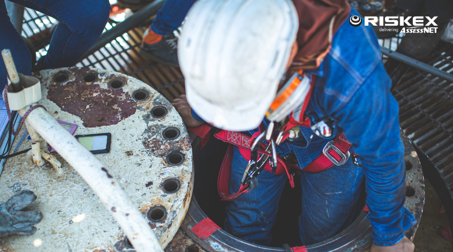 Worker in a confined space climbing into a tank with harness and hardhat.