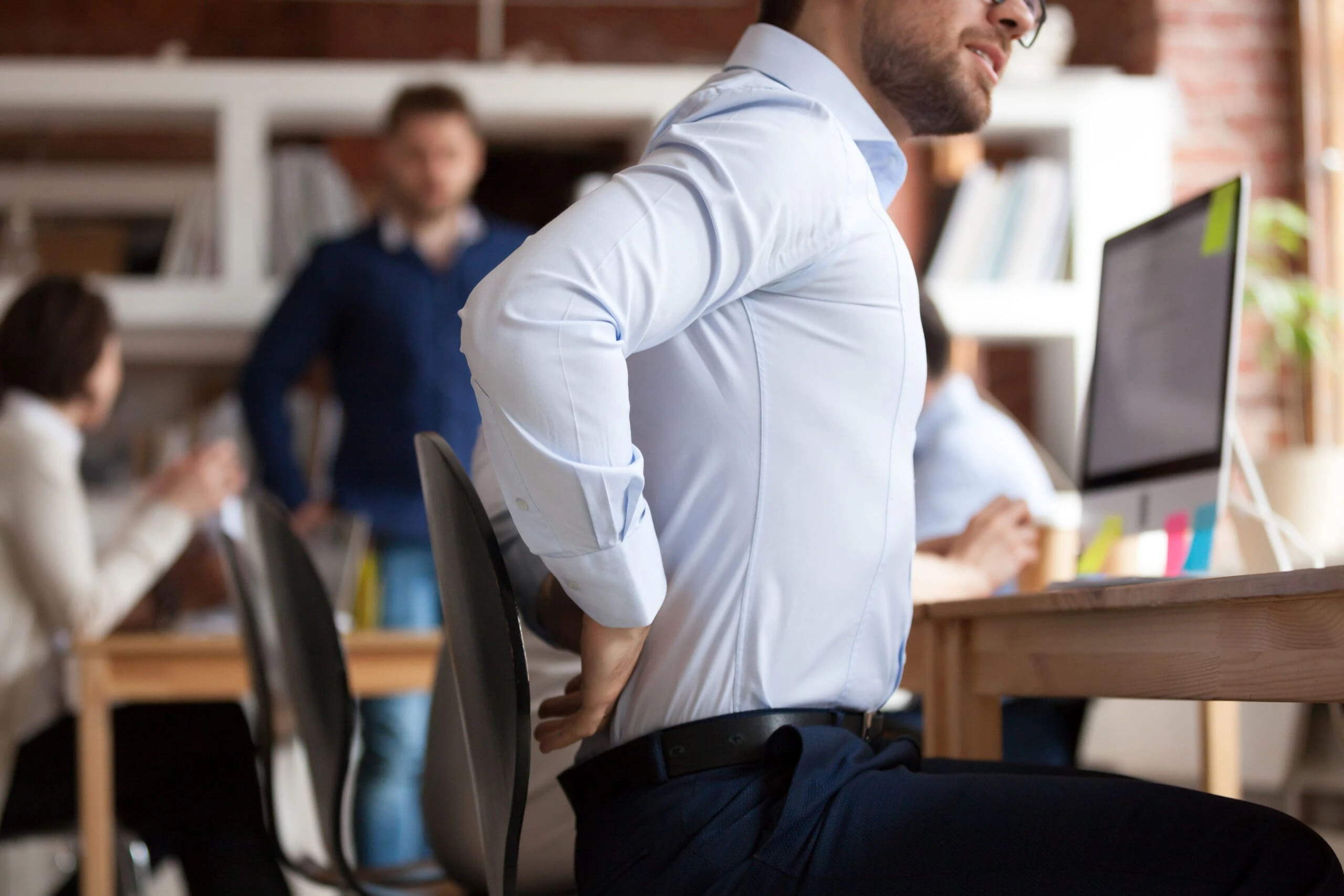 Man holding his back whilst sitting at a work desk.