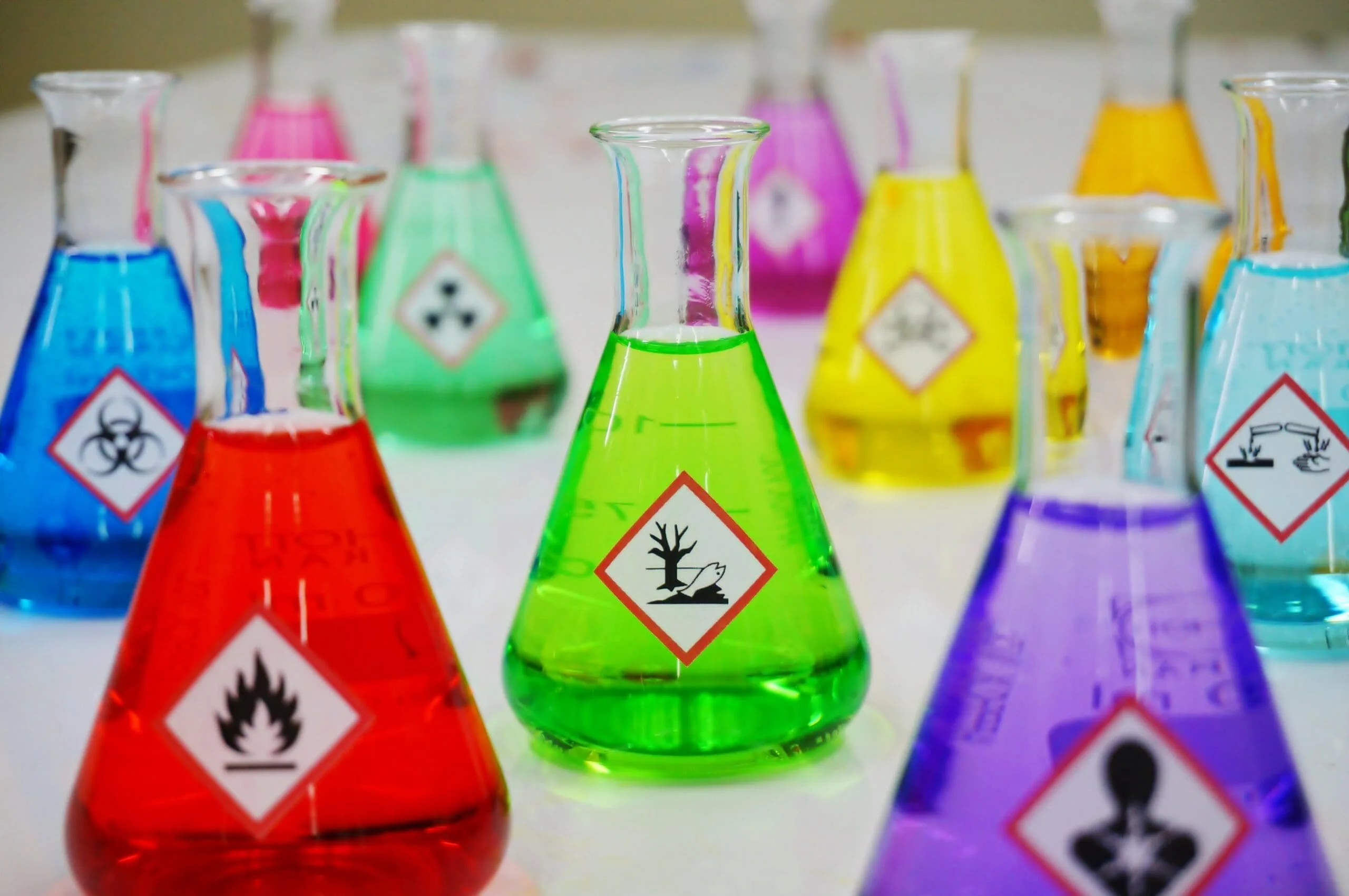 Science flasks with chemical warning labels in a multitude of bright colours - green, purple, red, blue, yellow.