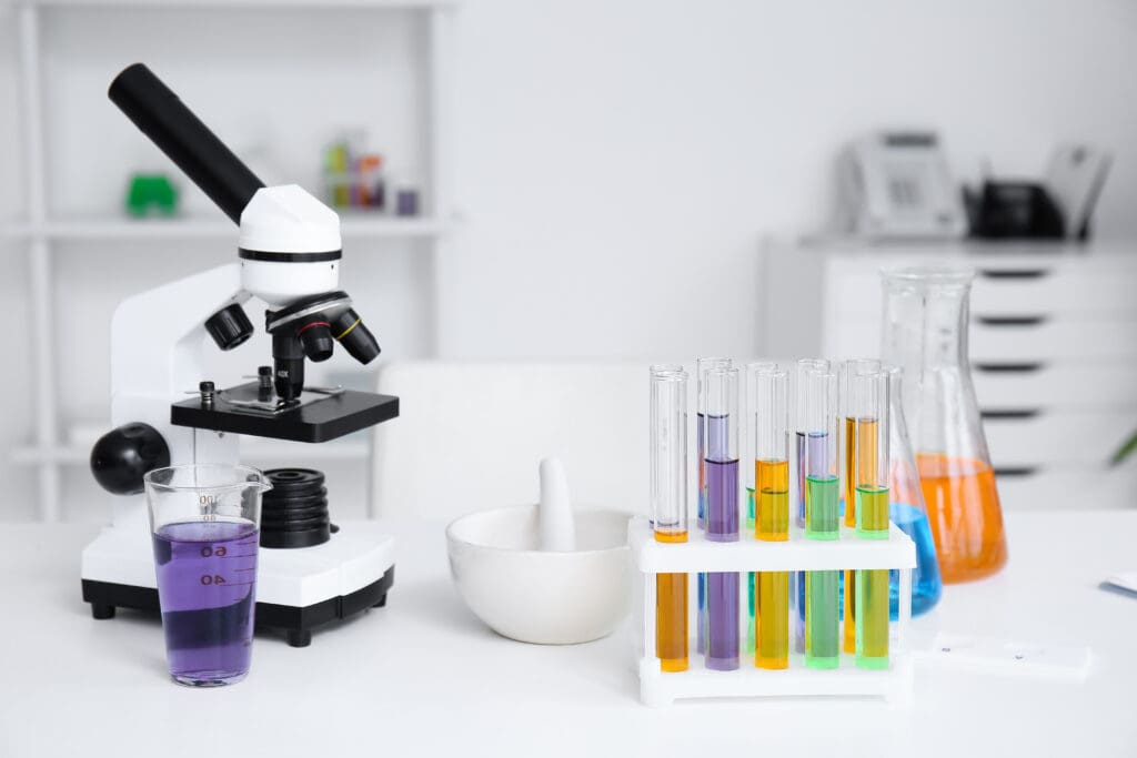 Modern microscope and colourful chemical glassware on table in medical laboratory.