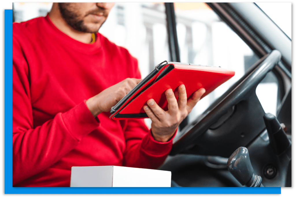 A man in a red sweatshirt sitting in a van using a red tablet.