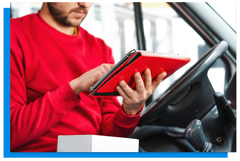 A man in a red sweatshirt sitting in a van using a red tablet.
