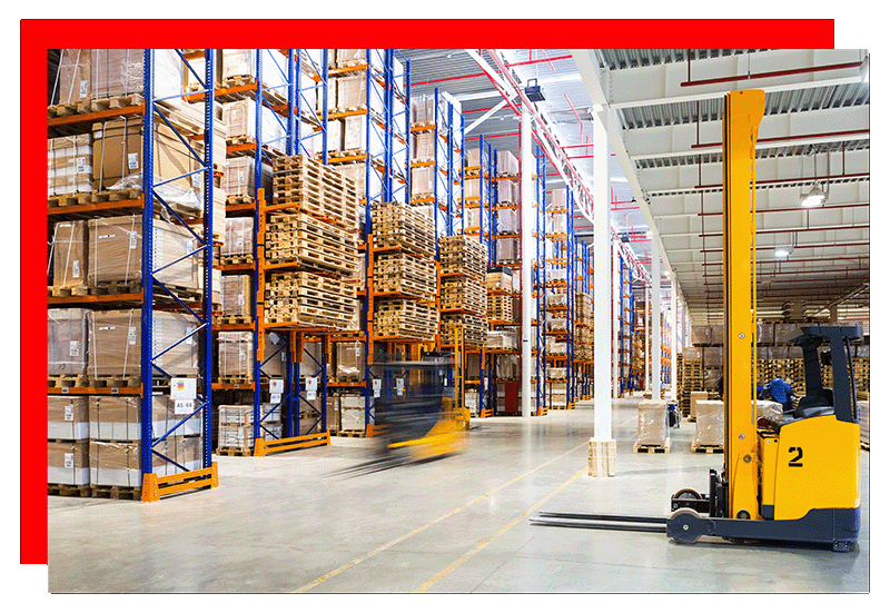 A warehouse with floor to ceiling racking and two yellow forklifts.