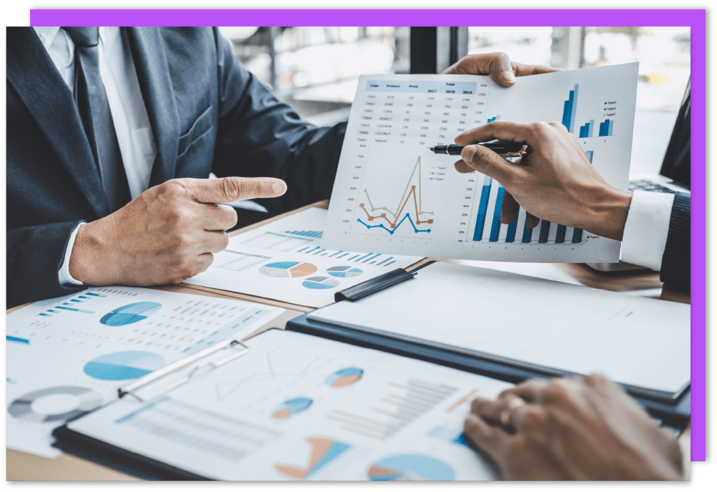 Two people in suits discussing paperwork with charts, graphs and data.