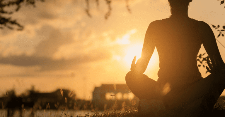 a person sitting in the grass meditating with the sun in the background