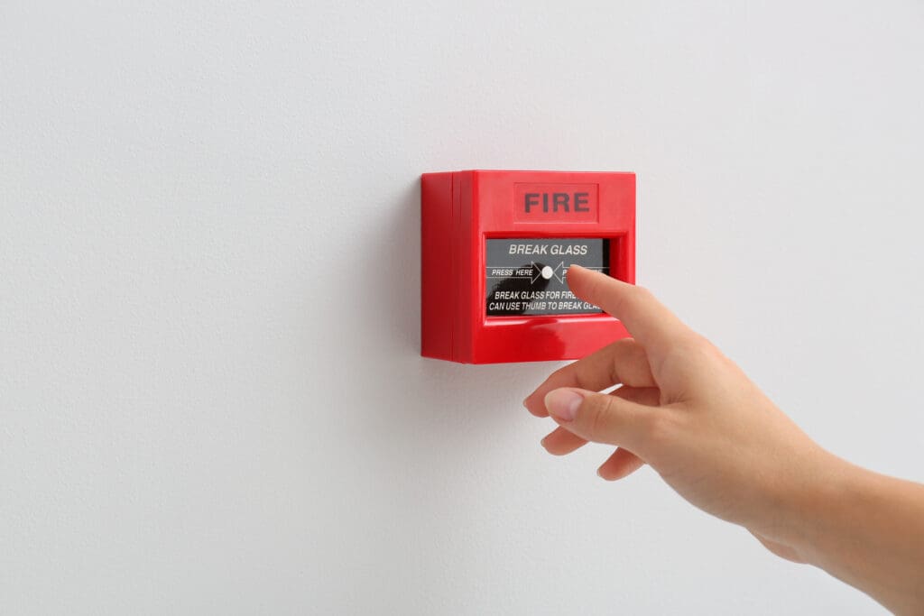 A hand going to press the fire alarm button panel.