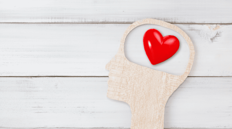 Human Head and Red Heart inside brain shape over white wood background.