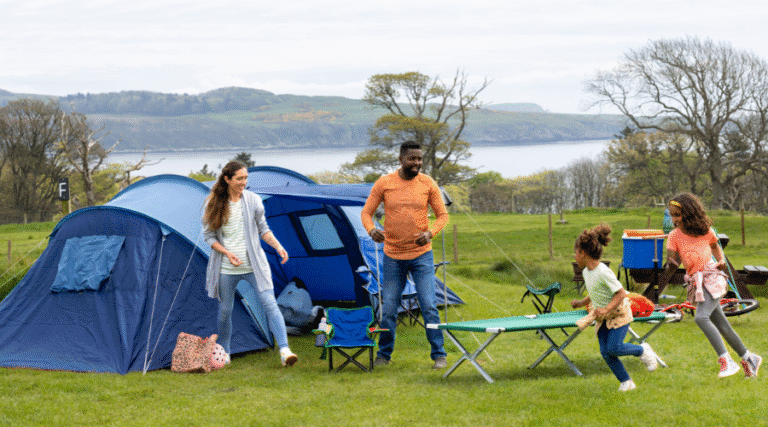 A tent camping setup with a family , two children running around having fun.