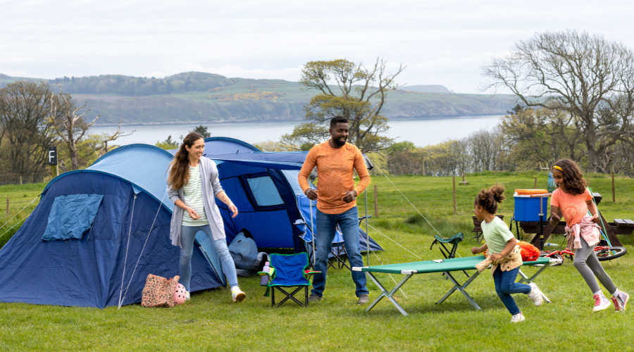 A tent camping setup with a family , two children running around having fun.