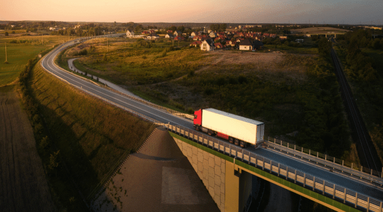An aerial photograph of a white and red lorry driving on a motorway bridge.