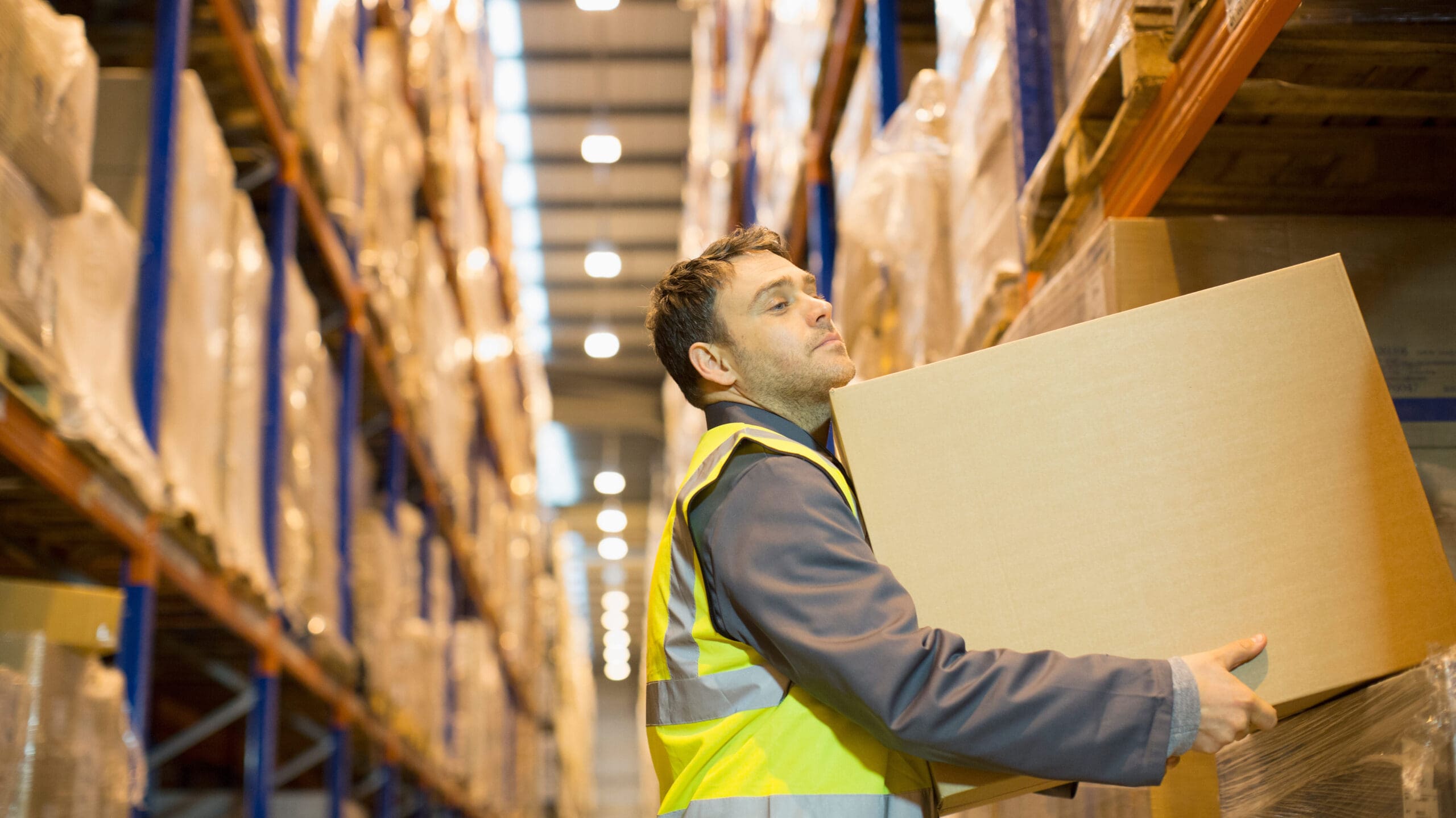 Man in a warehouse in a hi vis lifting a box.