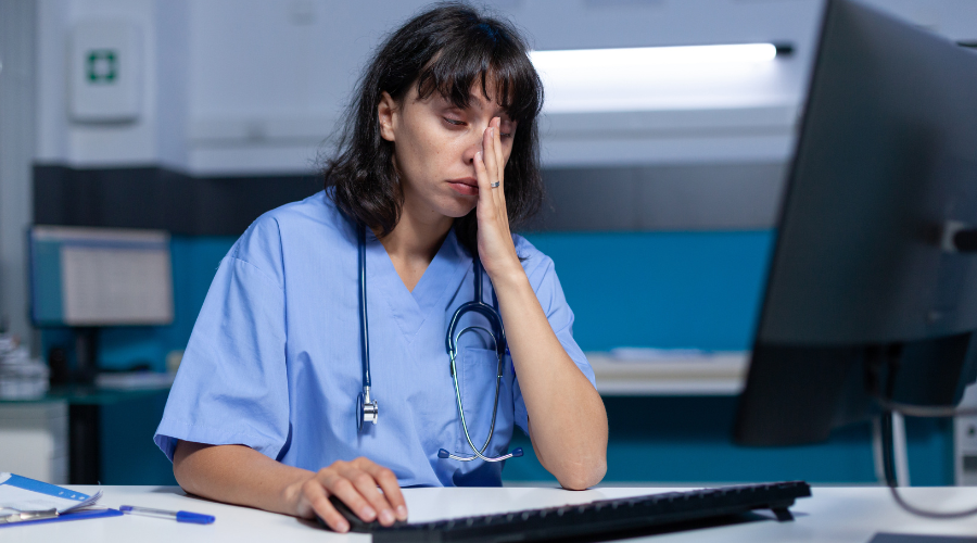 Woman Nurse Using Monitor on Desk, feeling Exhausted.