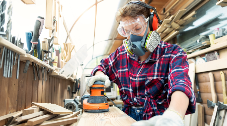 Female Carpenter Grinding Raw Wood with Orbital Sander Tool in a workshop.