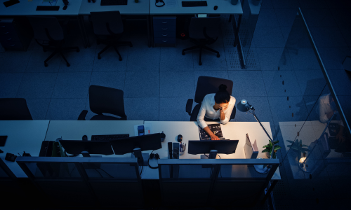aerial view of a lady working late at the office in the dark with a lamp just illuminating her desk.