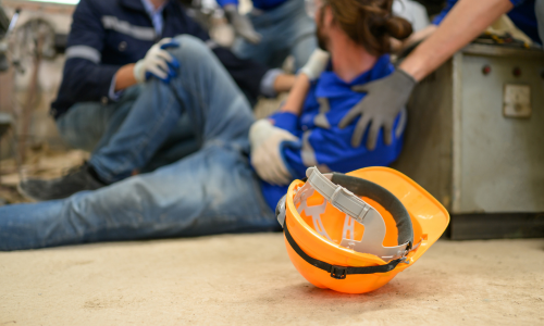 man on the ground after falling in a warehouse and a hard hat on the floor in front of him.