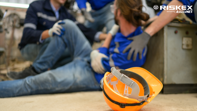 man on the ground after falling in a warehouse and a hard hat on the floor in front of him.