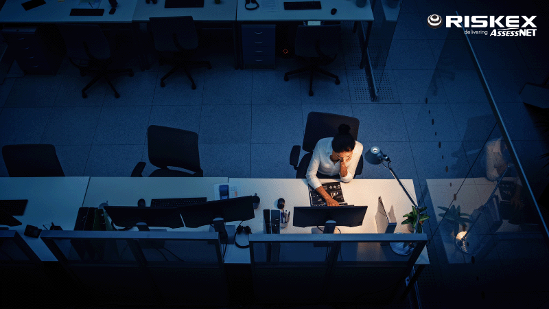 aerial view of a lady working late at the office in the dark with a lamp just illuminating her desk.