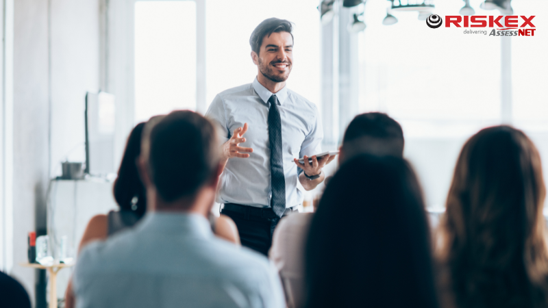 Man presenting to a group of people in business attire carrying a tablet.