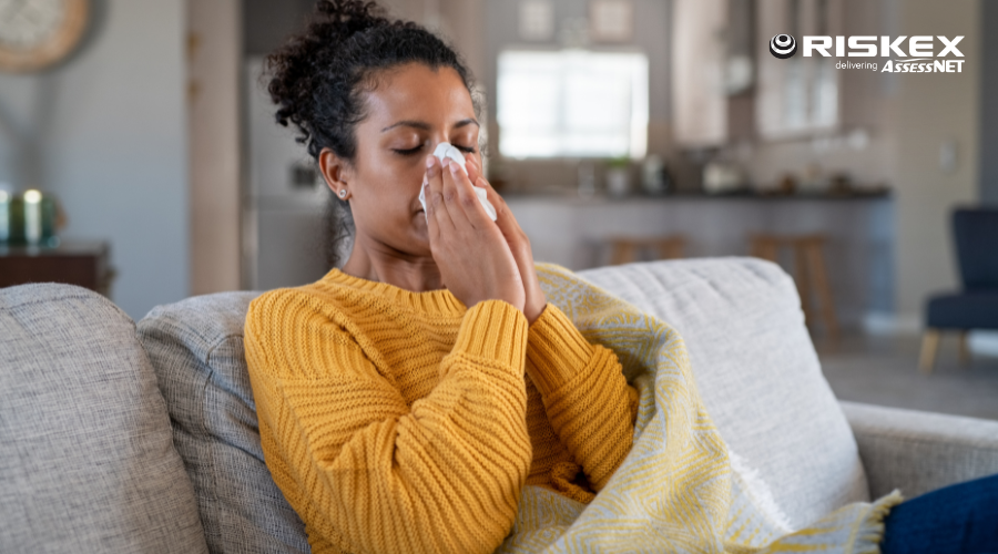 woman sat on the coach blowing her nose wrapped in a blanket.