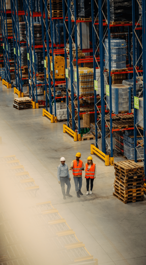 three people in hard hats and hi vis vests in a warehouse.