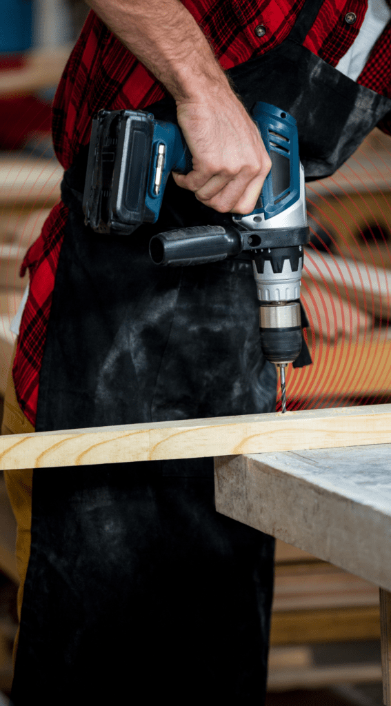 Main using a drill on a plank of wood.
