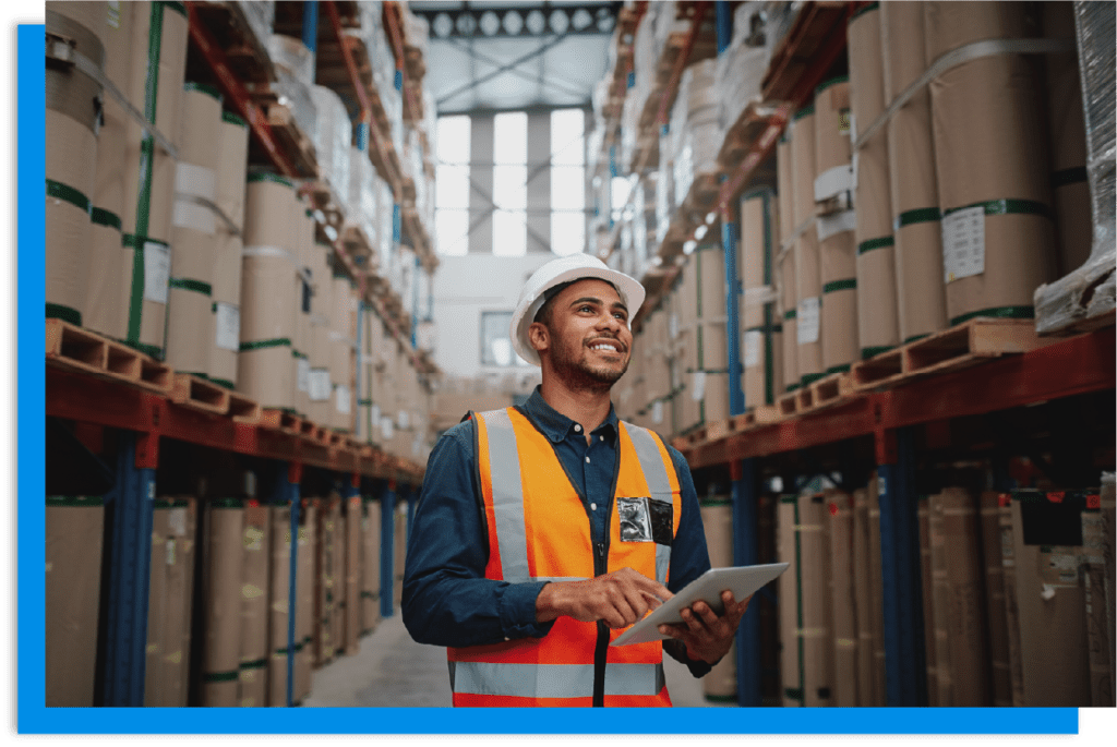Man in PPE in a warehouse holding a tablet.