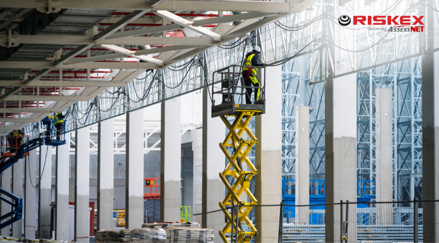 Construction workers using scissor lifts to carry out work at height inside a large industrial building.